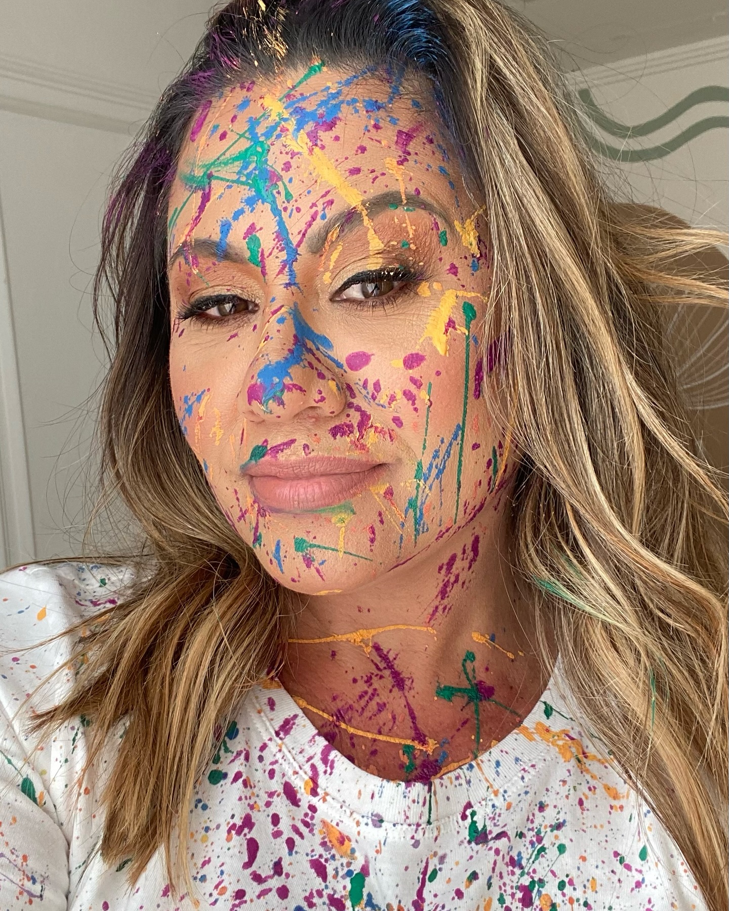 Karina Costa com o rosto coberto de respingos de tinta colorida